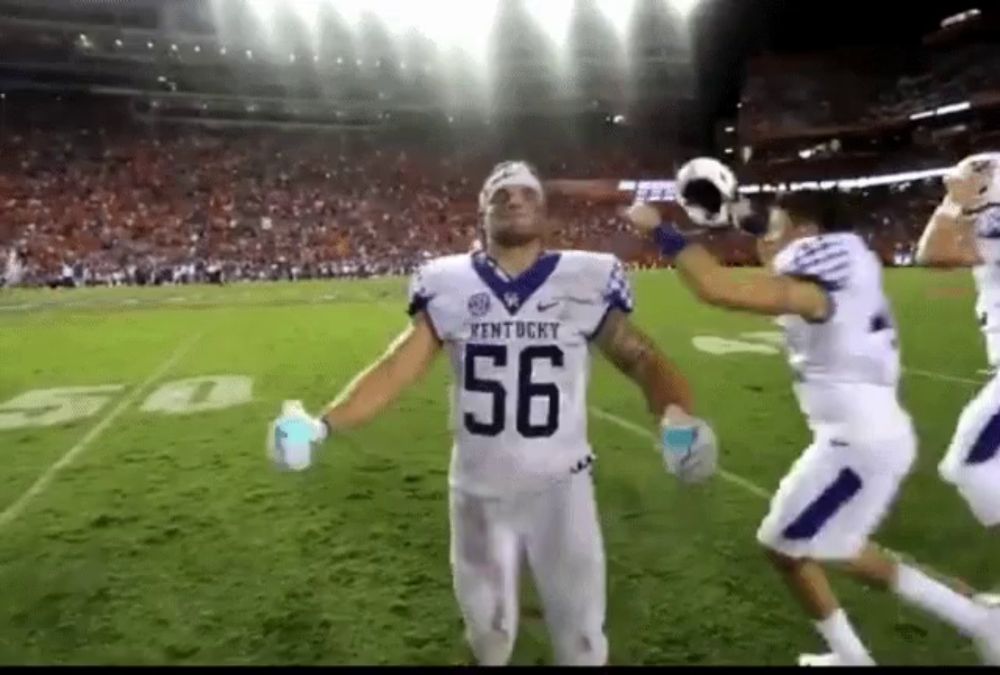 a kentucky football player wearing number 56 celebrates on the field with his teammates