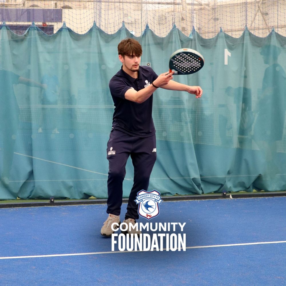 Young male playing padel tennis indoors, wearing navy coloured Community Foundation uniform.
