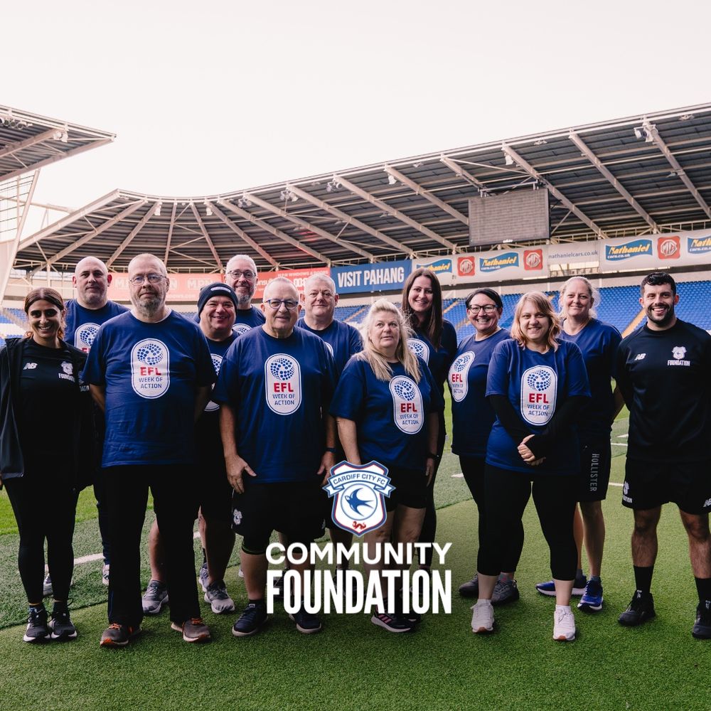 Photo shared by Cardiff City FC Community Foundation showing 10 people standing on Cardiff City FC pitch at Cardiff City Stadium in EFL branded t shirts.