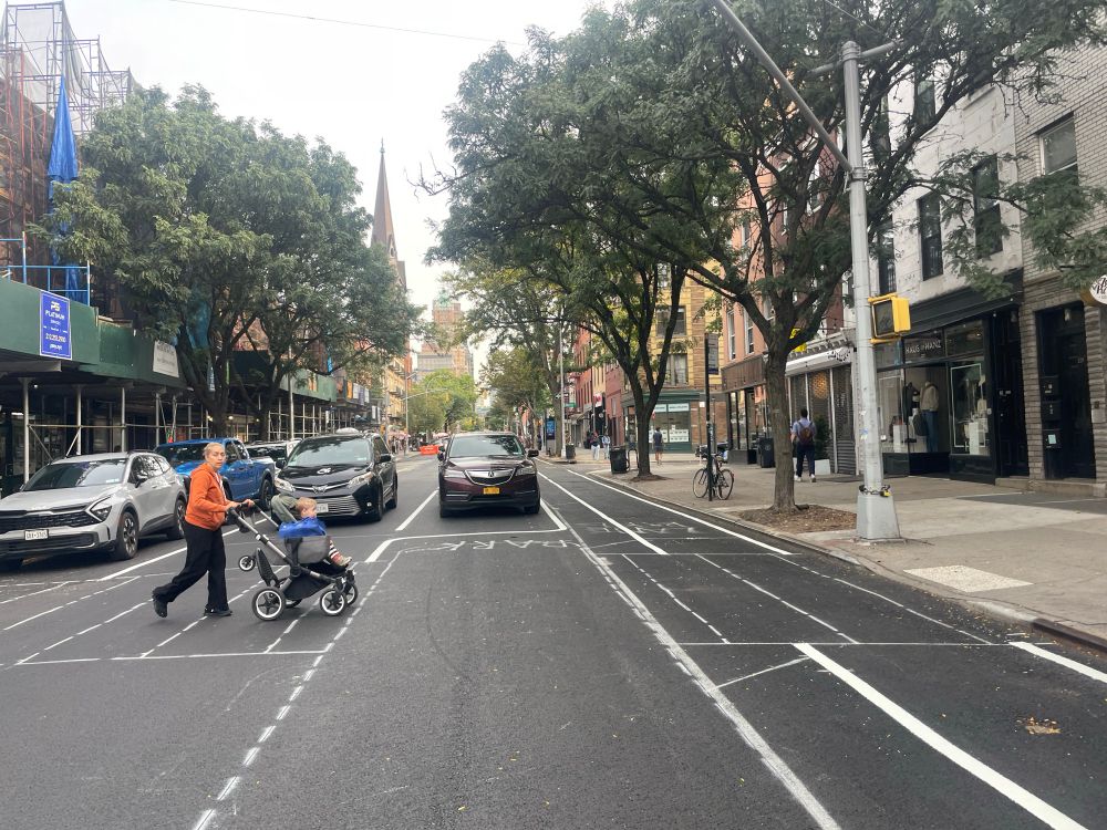 A woman with a stroller crosses an intersection of Court Street with partial markings in place for the new protected bike lane design. 