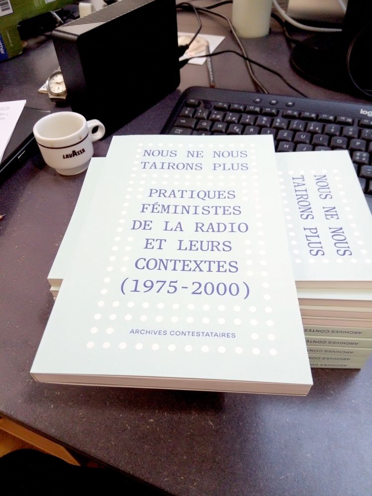Une pile de livres Nous ne nous tairons plus. Pratiques féministes de la radio et leurs contextes (1975-2000). La couverture est bleu-vert clair avec des points blancs qui évoques un haut-parleur. Au fond un clavier et une tasse de café.