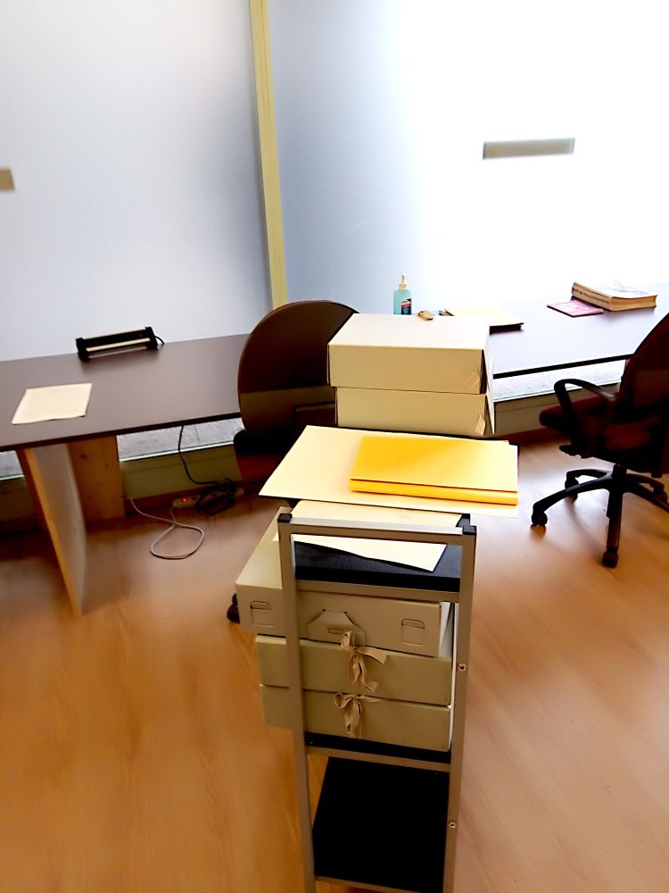 Intérieur de la salle de lecture. Au premier plan un chariot de bibliothèque et à l'arrière plan les postes de consultation.