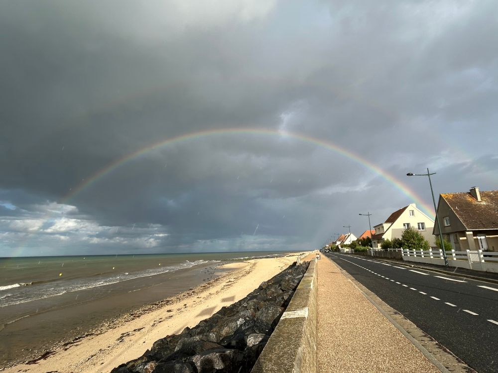 Doppelter Regenbogen über dem Meer, dem Strand und der Straße zu den Häuser