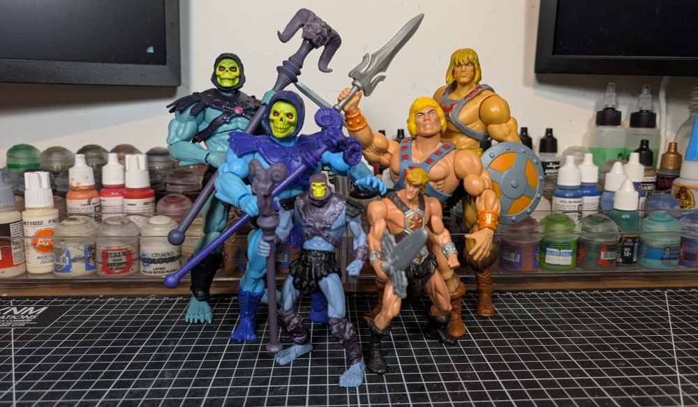 Toys on desk with cutting mat and paint racks, with 2 monitors in background