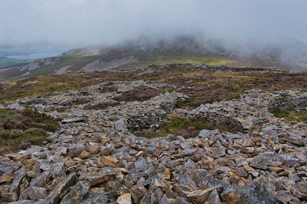 Low stone walls of round houses on a hill against a cloudy backdrop