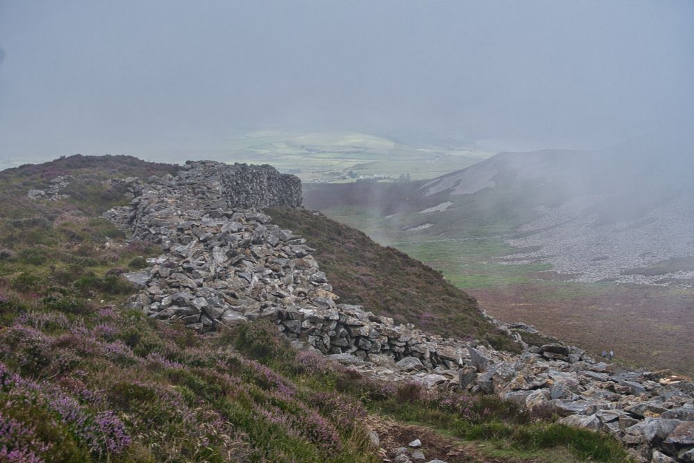 The stone rampart of a hillfort against a cloudy backdrop