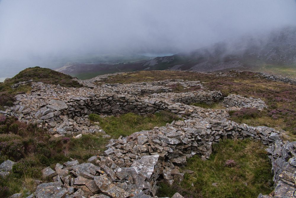 Low stone walls of round houses on a hill against a cloudy backdrop