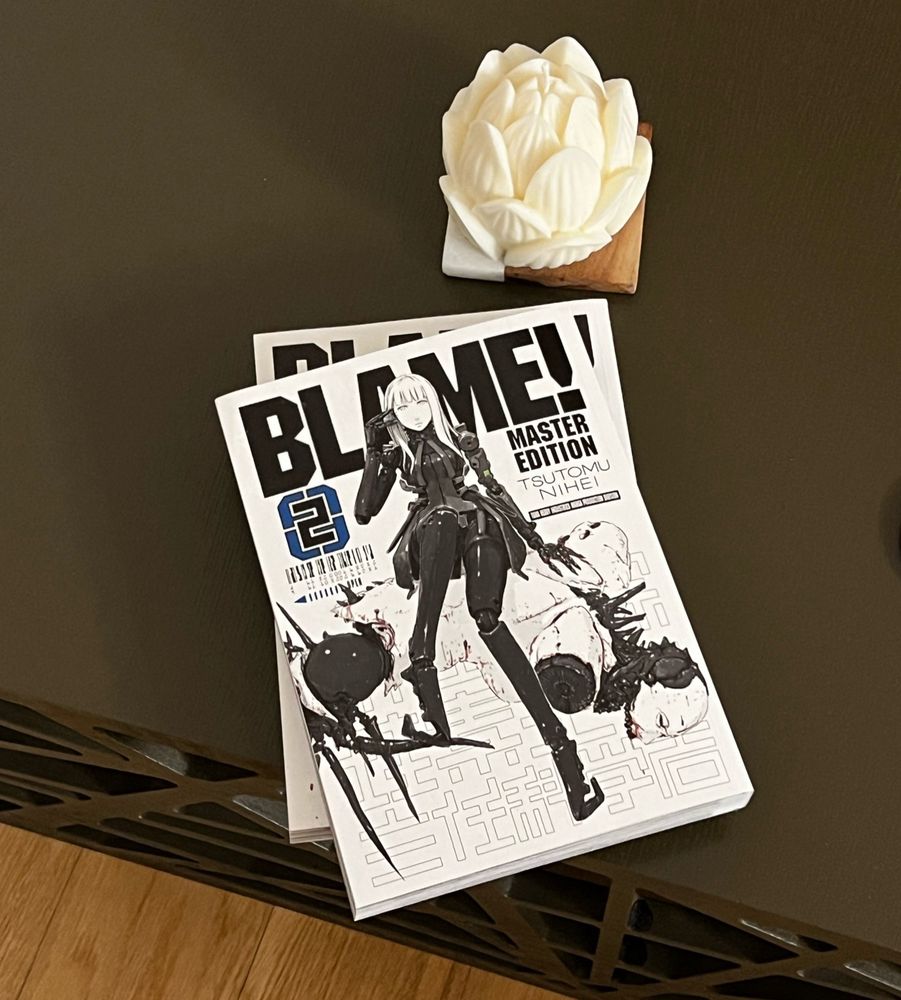Two manga books on coffee table near candle. Book is titled "Blame!".