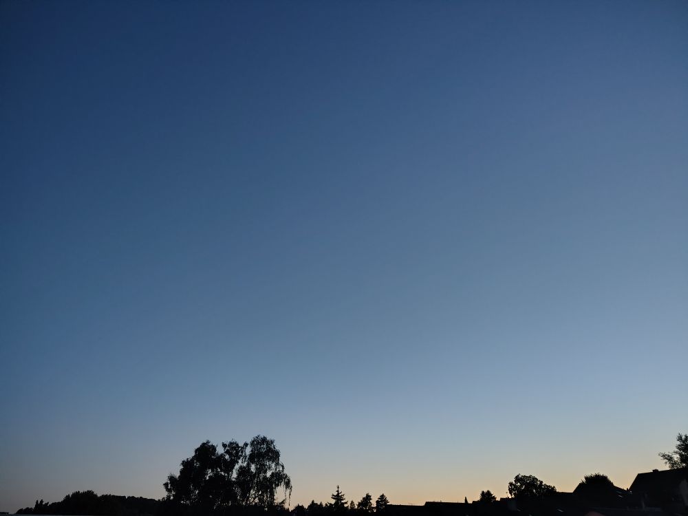 Abenddämmerung, am unteren Bildrand sind Bäume und Hausdächer zu sehen.