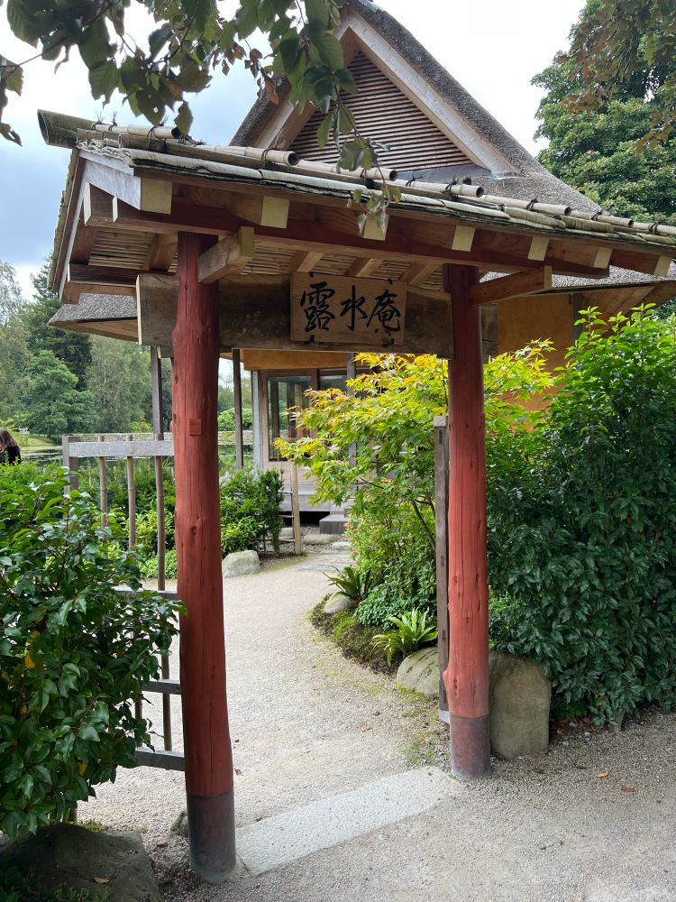 A coveted gateway leads to a path taking you further into the garden. Delicate bamboo dancing and hedges flanked by the gateway. The gateway cover is a pitched roof constructed in wood and bamboo. Japanese characters on the gateway roughly translate as ‘dew water healing’ – I think!