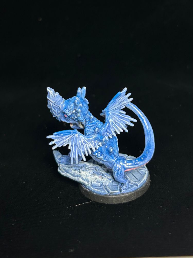 A figurine of a little blue dragon with a pink belly on ice against a black background.