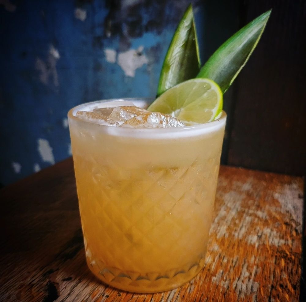 The described cocktail in a rocks glass, garnished with pineapple fronds and a lime wheel 