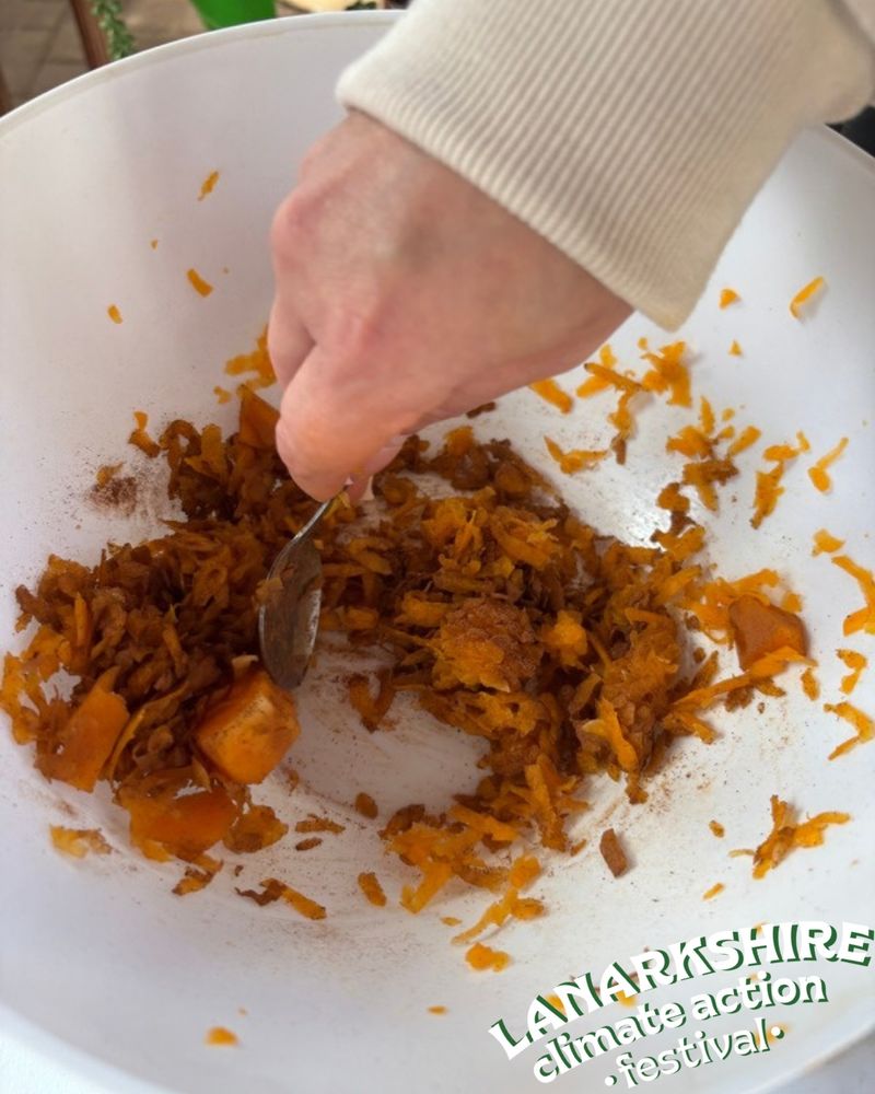 A hand using a spoon to mix together vegetables in a bowl.