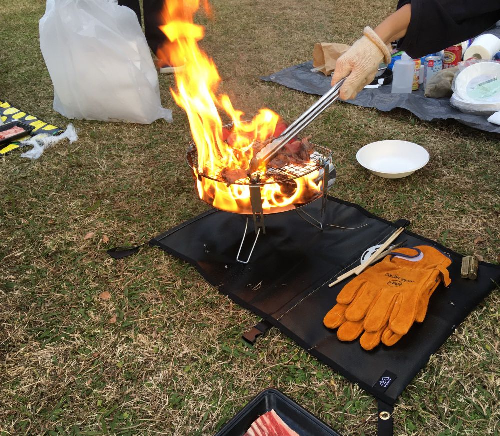 芝生のうえr。金網の上で肉を焼く人。

炎立ち上がり、肉を焼き尽くしそうな勢いで燃えている。