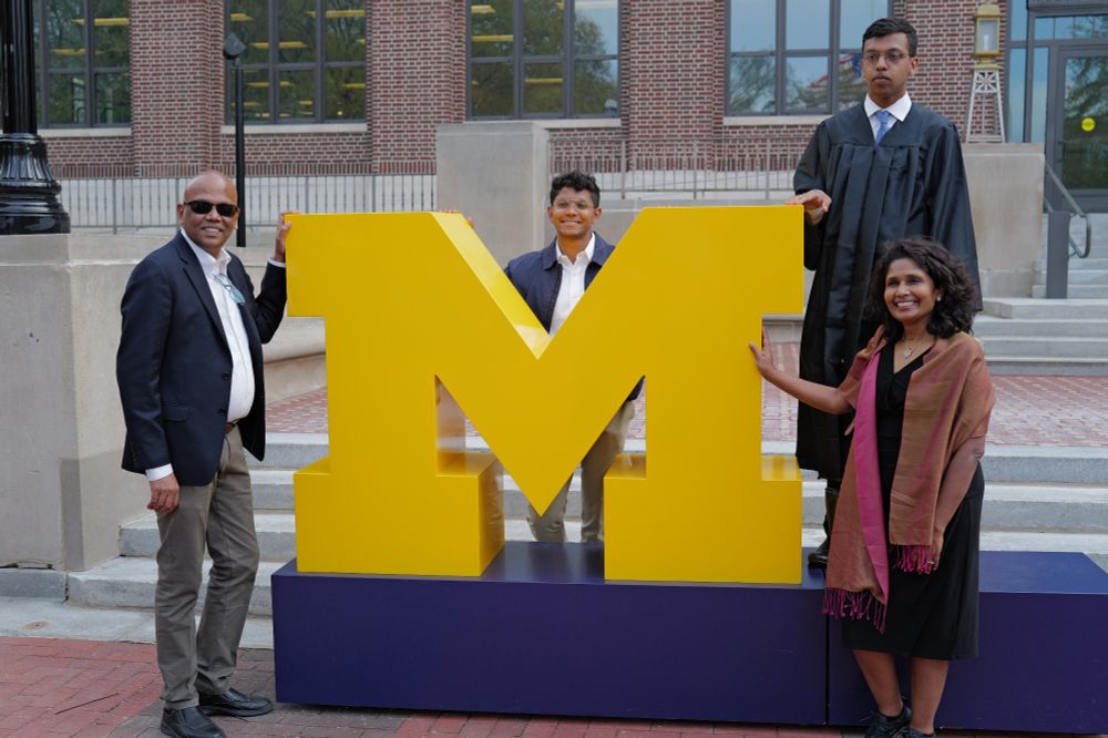 Family of four around a giant Block M in front of the Hatcher Library.
