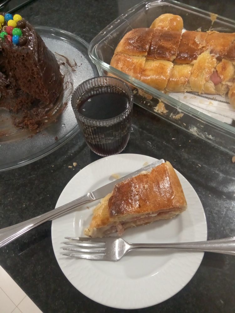 A picture of a slice of stuffed bread next to the whole loaf, a glass of coke and a chocolate cake cut in half