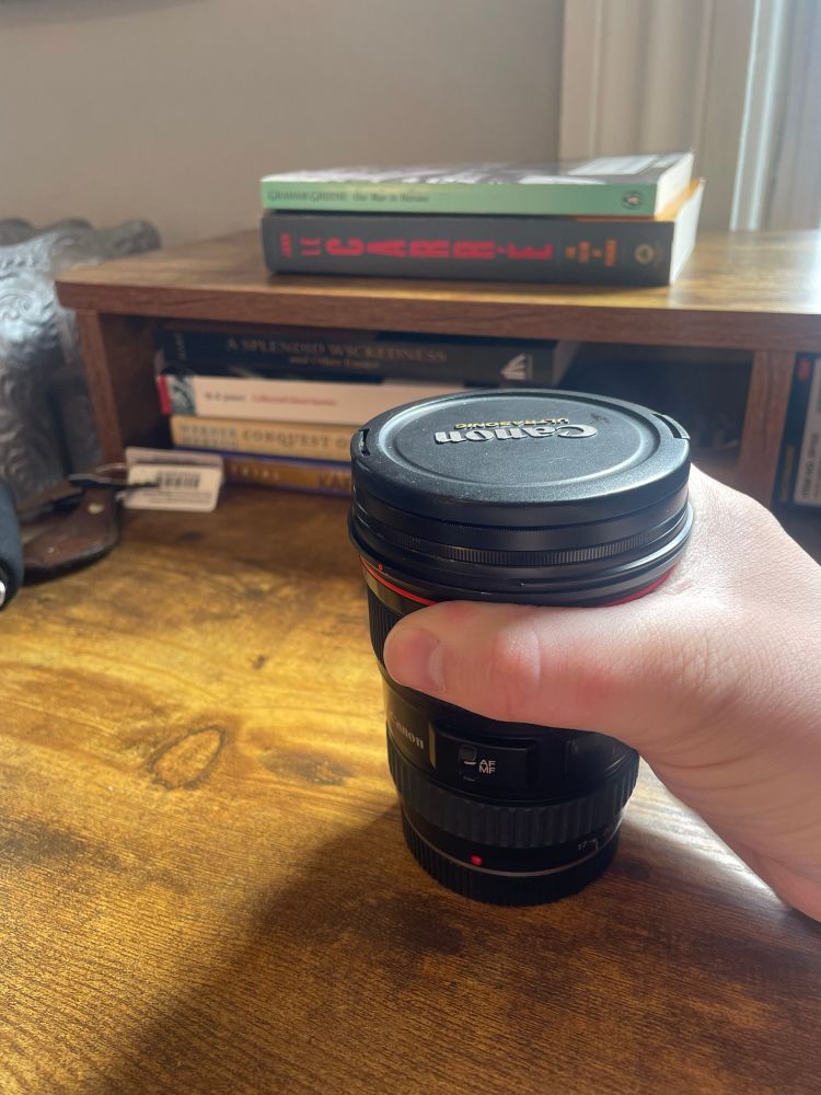 A 17-35mm Canon zoom lens in my hand on a wooden desk, with books in the background.