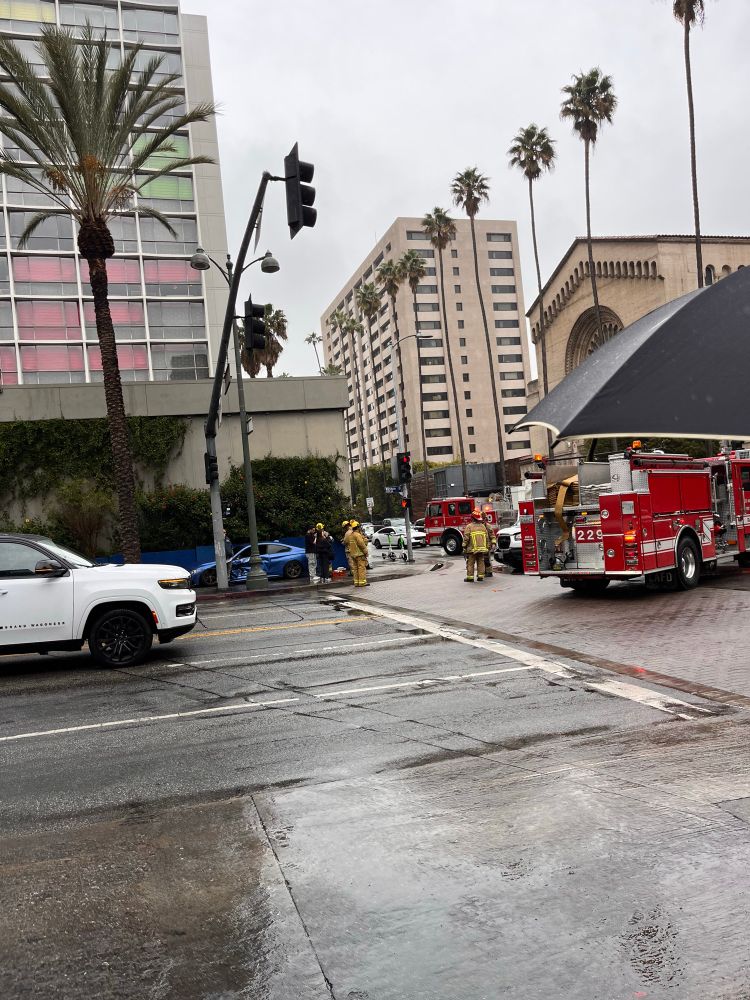 A photo of a car crash on a wet street in LA, fire trucks circle a smashed blue sedan