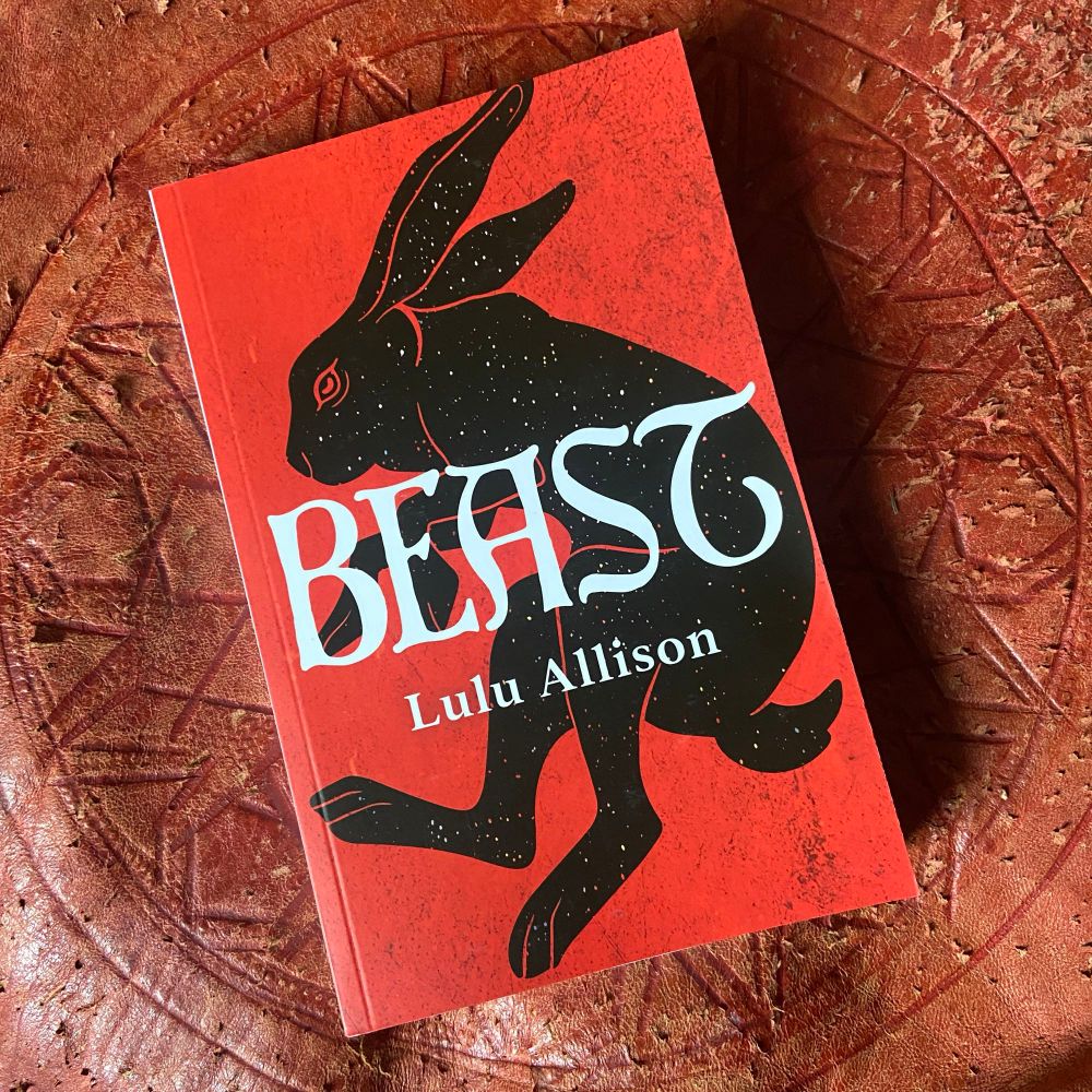 The book Beast (red background, cosmic rabbit in black, white font) on a red tooled leather pouf 