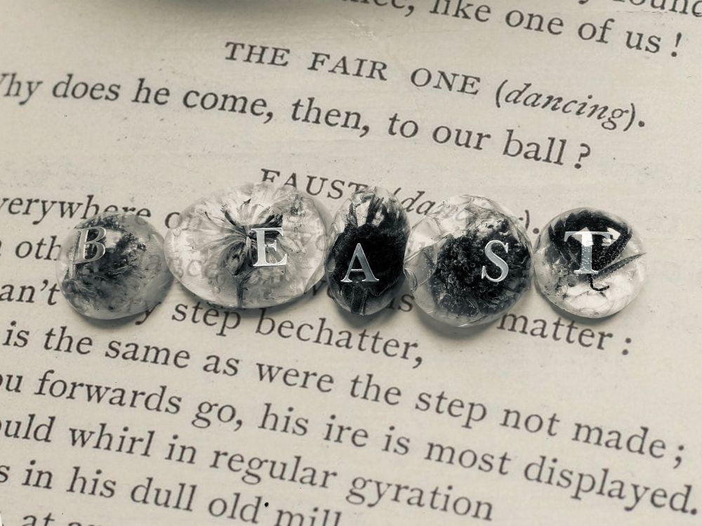 A page from Faust with 5 clear ovals on top. They contain flowers and snakeskin, each has a letter that spells out the word BEAST