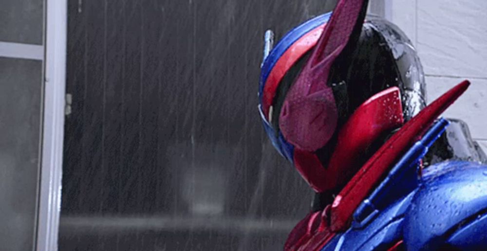 a red and blue superhero is standing in the rain wearing a helmet .