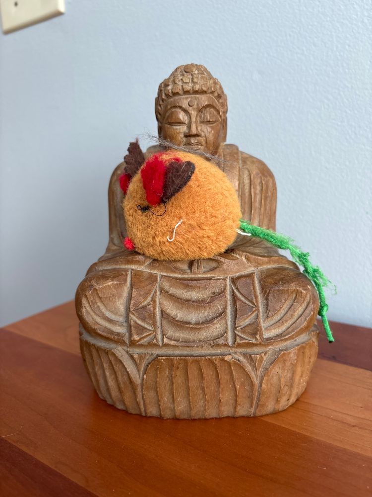 A well loved cat toy sitting in the arms of a wooden Buddha. A tiny lock of Torry-cat’s hair is atop of Mousey.