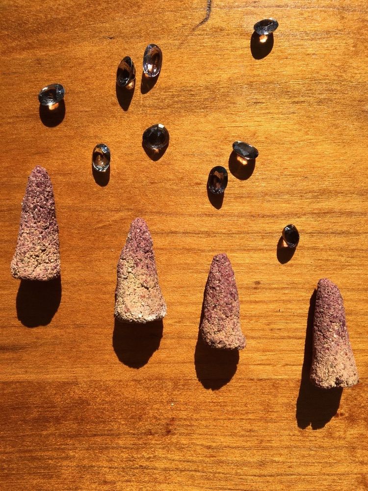 Chunky incense cones with pinkish tips on a sunlit cherry desk. Small gemstones are scattered above the incense.