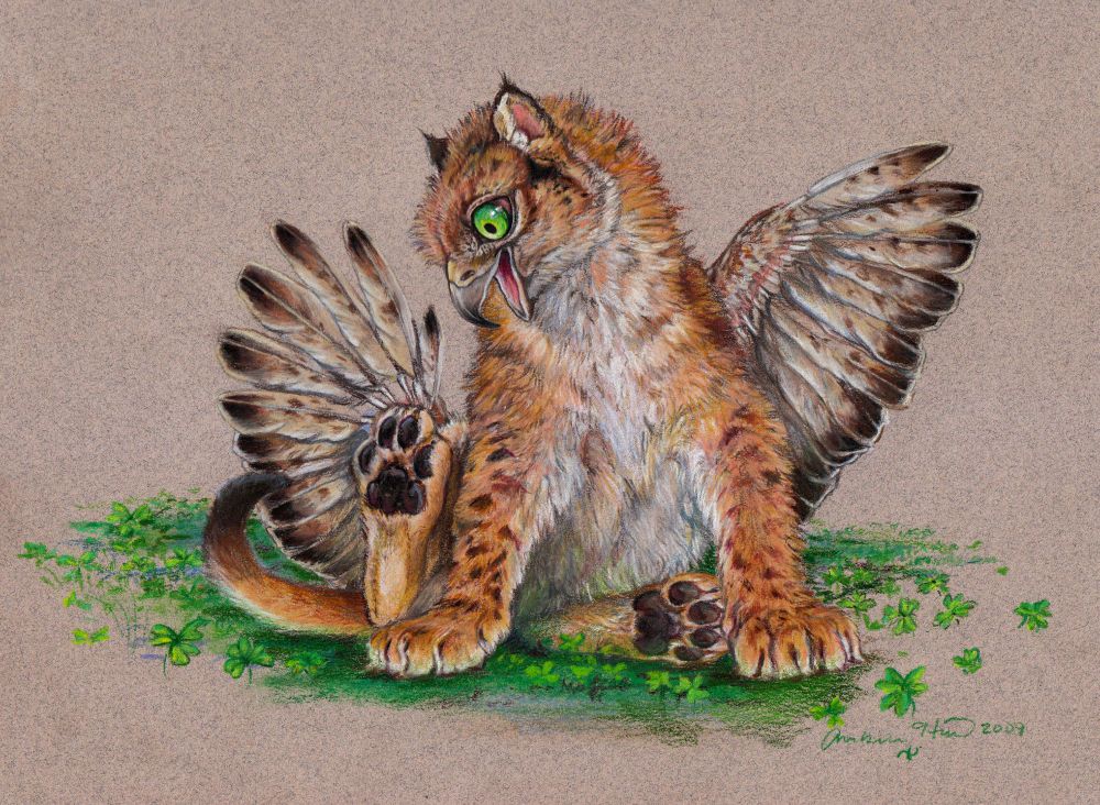 A young gryphon sitting on green clovers. One back foot is raised and he eyes it with glee, beak open in big grin, green eye alight with youthful joy. His wings are spread, the feathers still growing in with feather sheaths at the base. His tawny fluffy coat is spotted like a lion cub, his feather tips are dark, his ears are tipped with tarp pointy tufts. His toe beans are on full display.