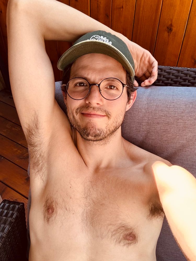 Picture of me shirtless, wearing a green cap and glasses. My arm is draped over my head. 
