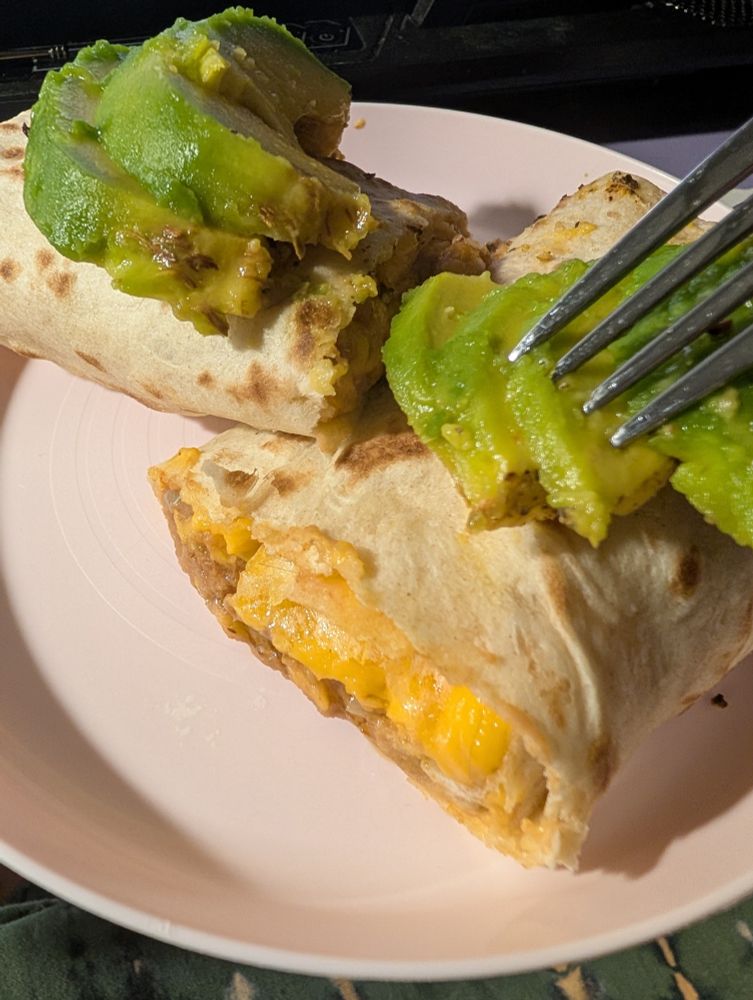 Bean and cheese burrito topped with avocado on a plate 
