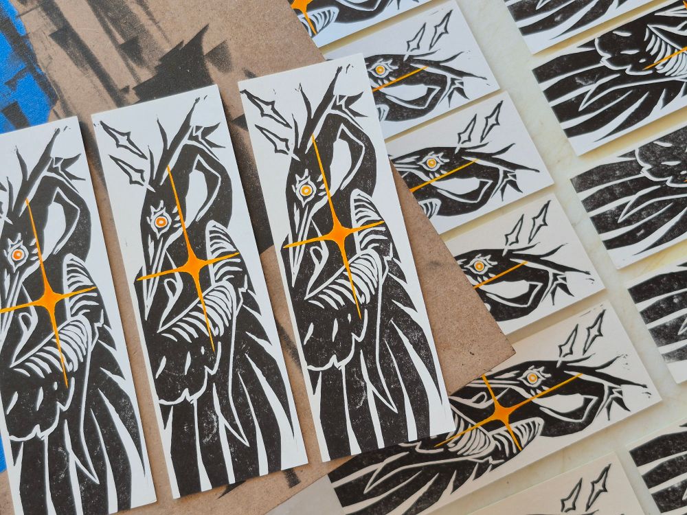 photo of hand printed bookmarks, showcasing a heron with a bright yellow star over its heart. its eye is a matching yellow.
