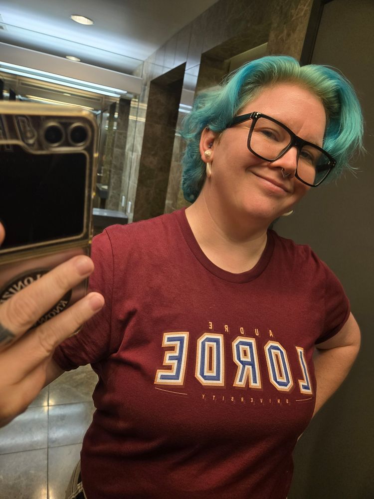 Non-binary person with blue-green hair wearing an Audre Lorde University t-shirt