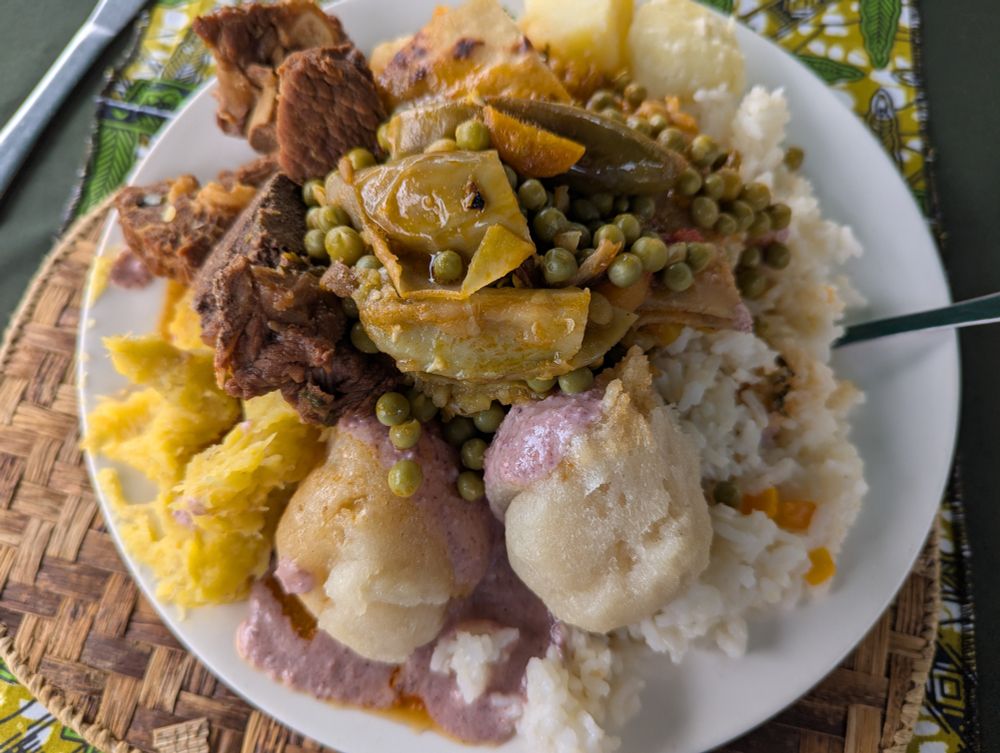 A plate of food with beef, peas and cabbage, yuca, pumpkin, white rice, fufu and peanut sauce, and mashed plantains.