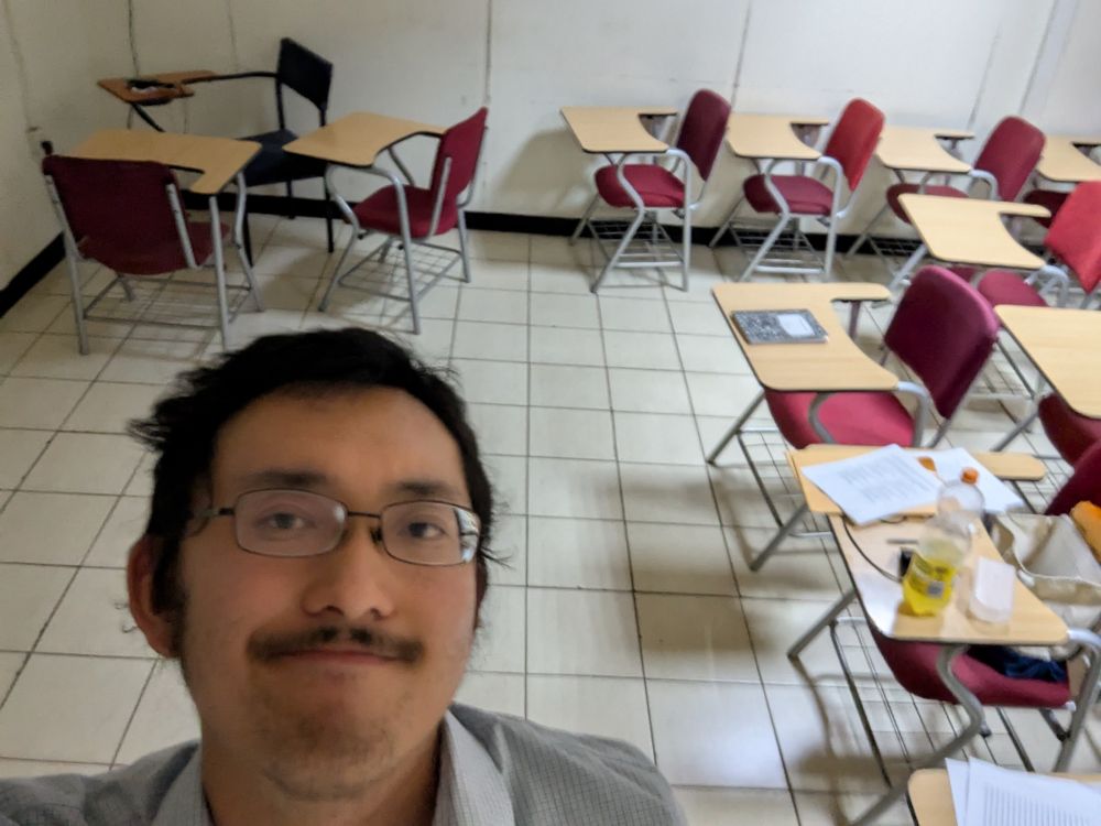 Me in a classroom looking tired with my hair messed up. Papers are strewn across desks and an audio recorder is in the corner.