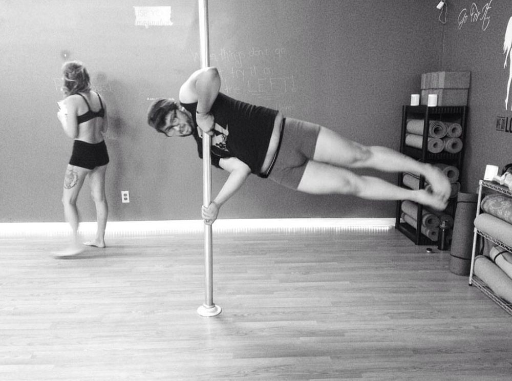 Beemz doing a half flag pose doing pole fitness. 