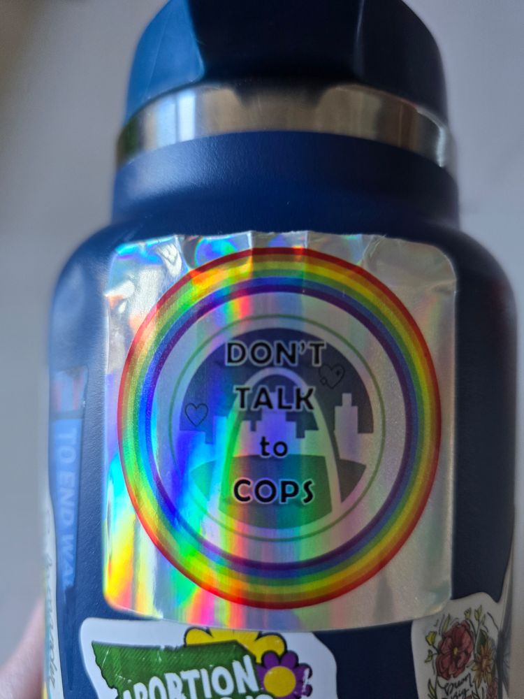 Reflective silver sticker with a rainbow circle and ArchCity Defenders logo with the words "DON'T TALK TO COPS" and v two hearts on a blue water bottle