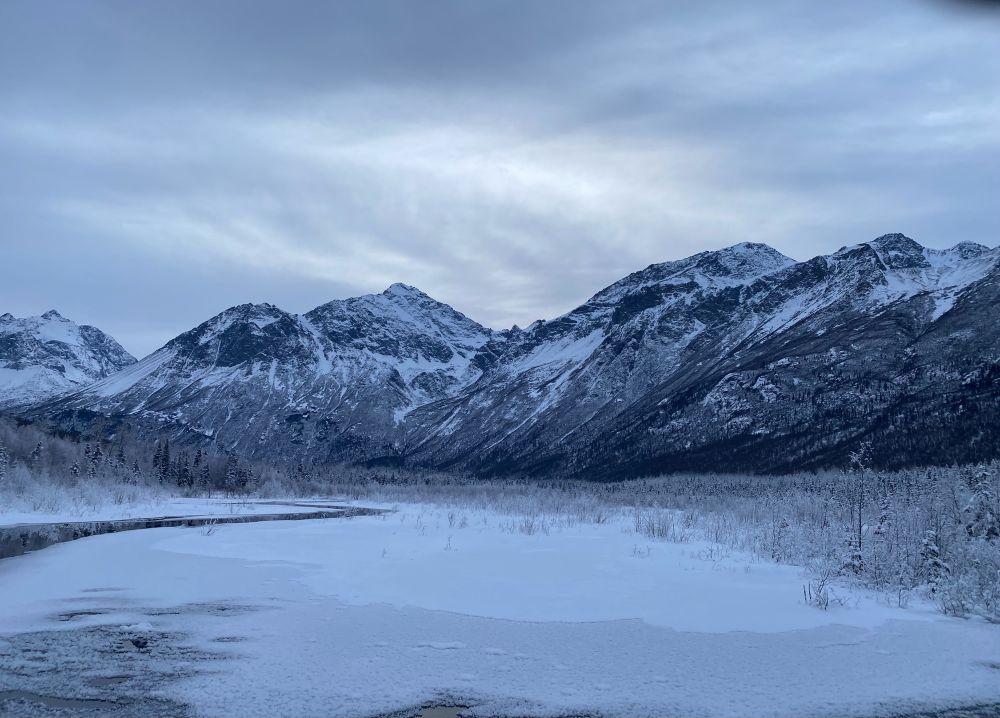 Valley with steep mountains in the background and a frozen river running through the foreground 