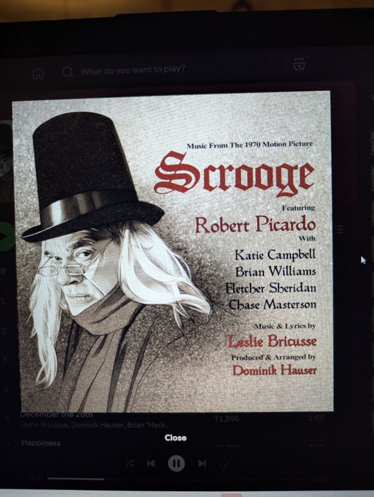A picture of Robert Picardo as Albert Finney's version of Ebenezer Scrooge. The text beside it says:
"Music From The 1970 Motion Picture
Scrooge
Featuring
Robert Picardo
With
Katie Campbell
Brian Williams
Fletcher Sheridan
Chase Masterson

Music & Lyrics by
Leslie Bricusse

Produced & Arranged by
Dominik Hauser