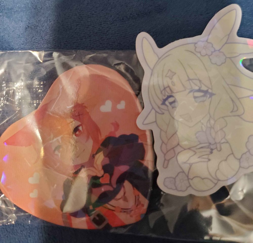 Very cute Scion Raha pin! He's giving heart hands! Also, the pin is very shiny!!! Next to him is a cute sticker that came with the pin. Also very shiny.