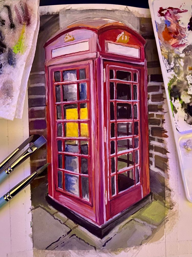 a photo of a rough guoache painting, of an old, British, red, telephone box in front of a brickwall background.  There are also, 3 paintbrushes, a paint palette, and a tissue covered in paint in the photo.