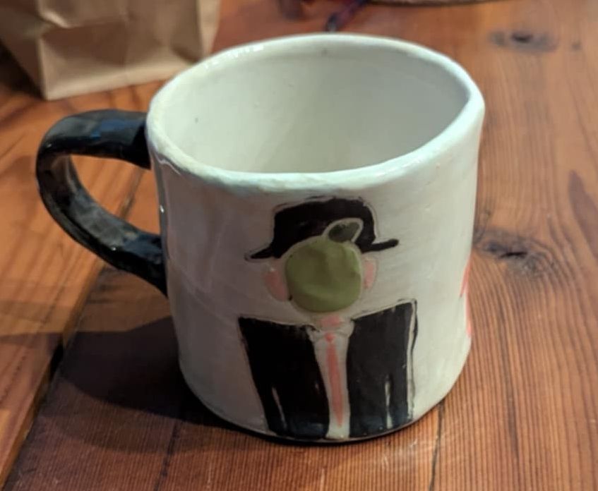 A mug with Magritte's Son of Man doodled into the surface 
