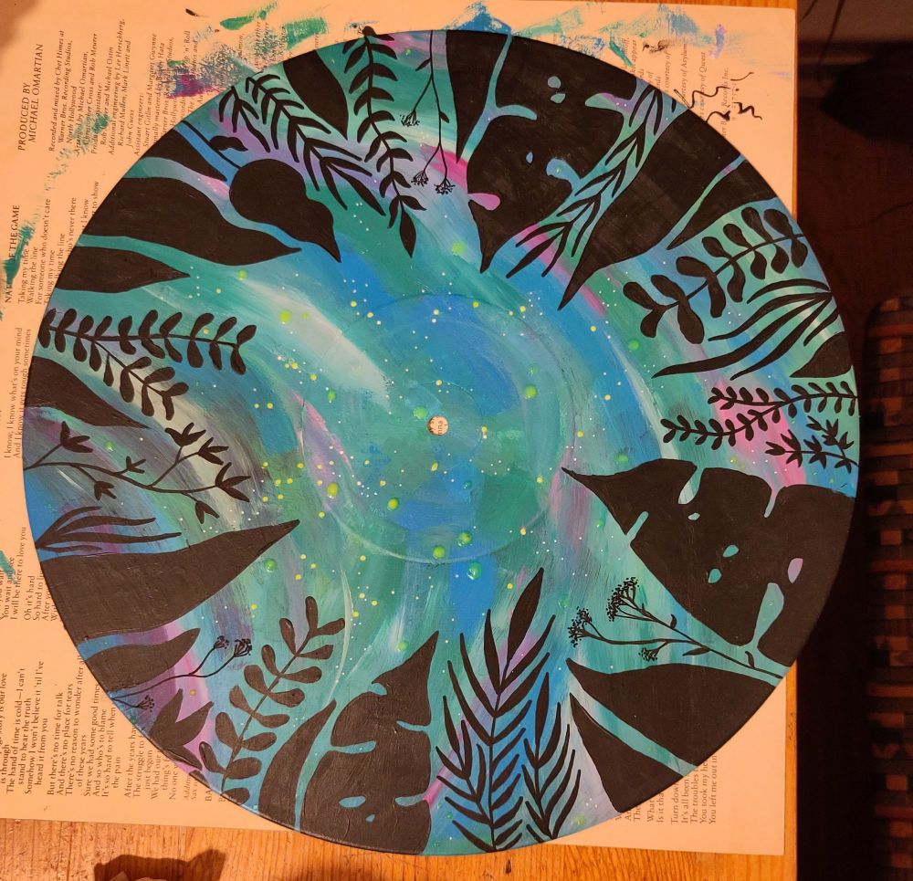 A phone of a painted vinyl with a colorful blue, green and pink background and the outlines of leaves are painted in black acrylic over it