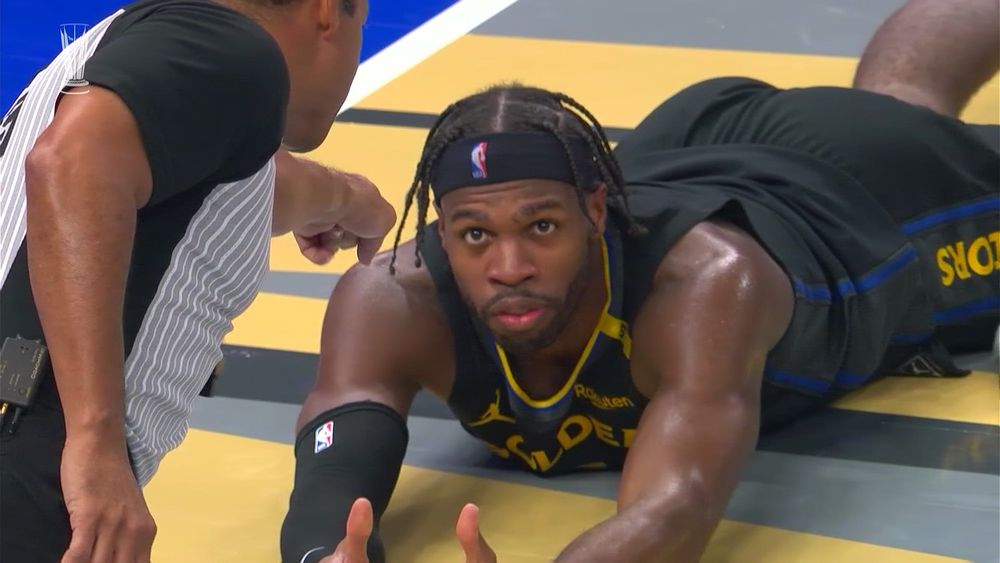 Buddy Hield lying on his stomach facing the camera with his arms up and a referee from the back pointing at Hield