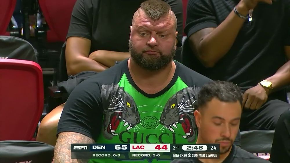 Sizeable man with a beard and pointed mohawk in a green Gucci shirt with black short sleeves that has panthers on both shoulders - think Zangief