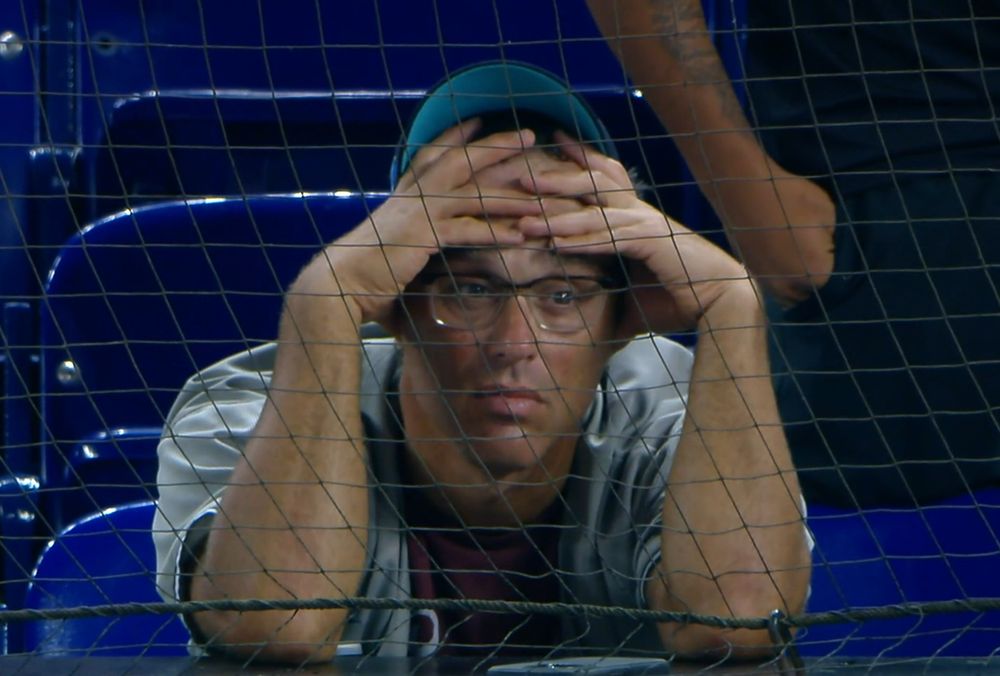 stressed fan in Miami with hat pushed up on his head leaning on his elbows with both hands on his forehead