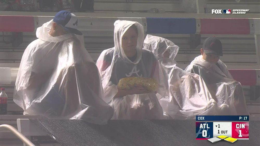 a family of very wet people wearing ponchos in the stands in Bristol for the Speedway Classic, there is a woman cradling a long bag of popcorn in her arms