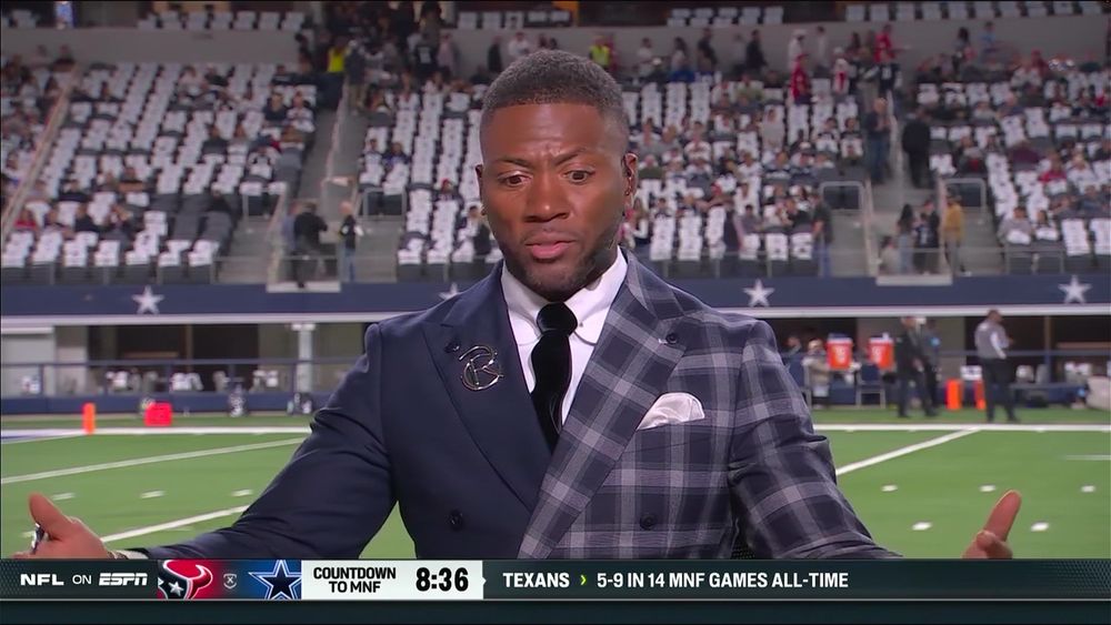 Ryan Clark on ESPN with his arms out in a white shirt with a black tie and a jacket that is half blue and half blue and white plaid