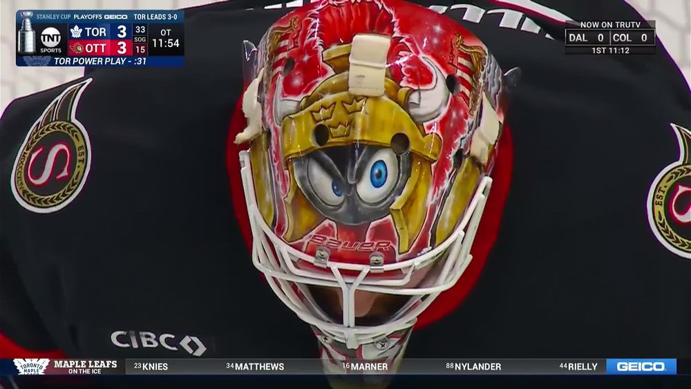 Top view of Linus Ullmark's mask as he looks down at the ice with Marvin the Martian doing the one eye cocked look, he has a red Senators comb on top of the helmet which also has horns and the tre kronor emblem for Sweden on the front