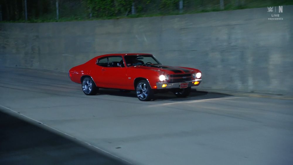 red 1970 Chevelle SS with black stripes coming down the concrete arena ramp with the lights on