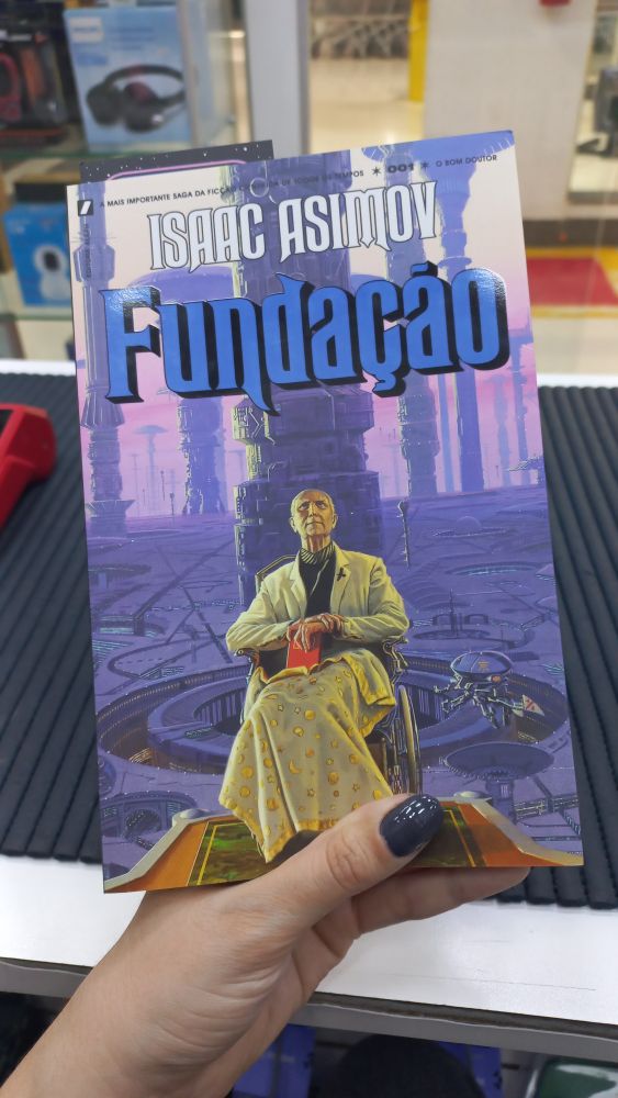 Capa do livro "Fundação" do Isac Asiminov

Descrição da capa: um idoso de roupa branca em uma cadeira de rodas com as pernas cobertas por uma manta infantil de espaço segurando um livro vermelho. Ao fundo uma cidade futurista de arquitetura peculiar